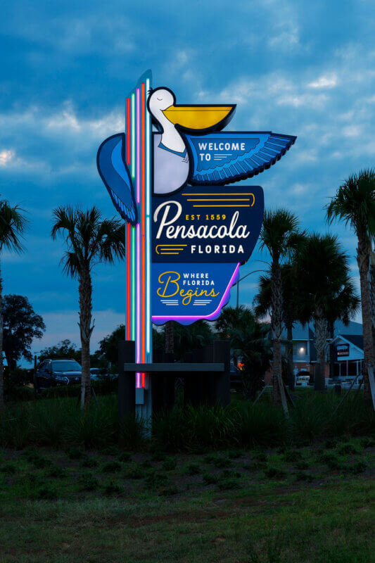 A shot of the "Welcome to Pensacola, Florida" sign at dusk, with the neon lights beginning to glow against the blue twilight sky.
