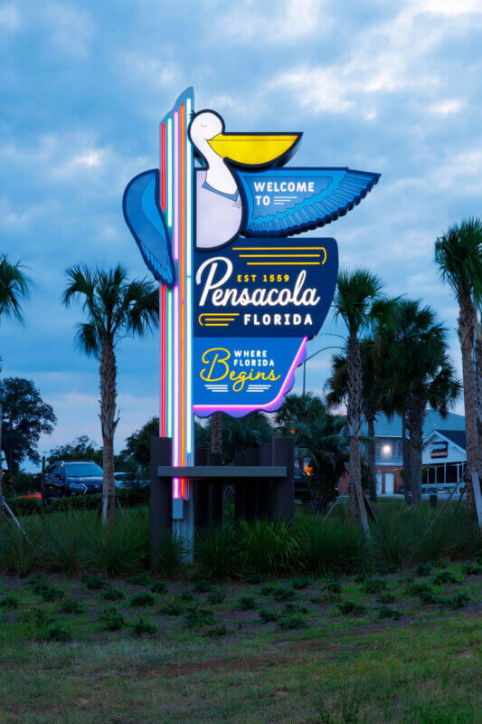 A shot of the "Welcome to Pensacola, Florida" sign at dusk, with the neon lights beginning to glow against the blue twilight sky.