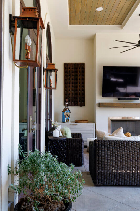 A cozy corner of an outdoor patio with a fireplace, television, and a small sitting area next to a potted plant and lanterns.