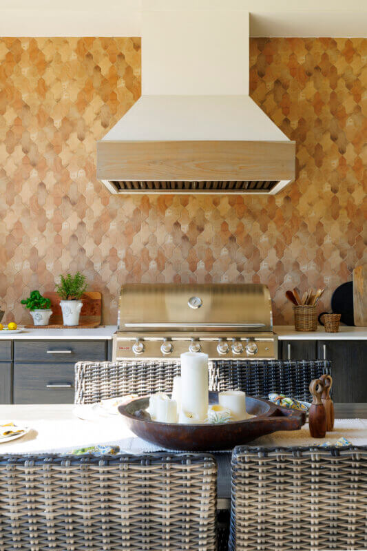 A close-up of a modern outdoor kitchen with a large stainless steel grill, a range hood with a wood accent, and a unique honeycomb-patterned backsplash.