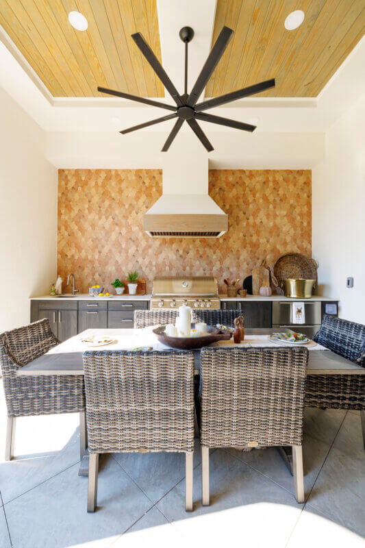 The dining area and outdoor kitchen on a covered patio, showing the full length of the table and the tiled backsplash.