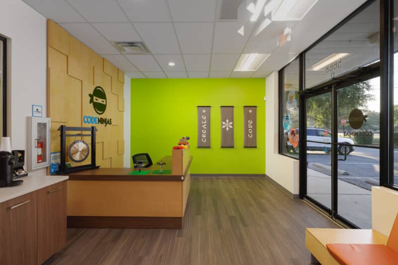 The vibrant lobby view highlights the lime green accent wall that serves as a high-energy backdrop for branded banners and the reception desk.