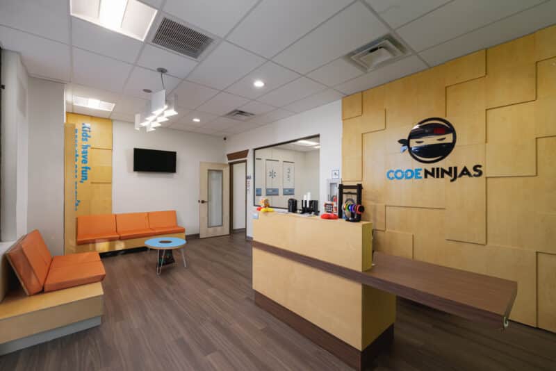 Code Ninjas Parent Waiting Lounge with orange benches, wooden display case, and exterior windows.