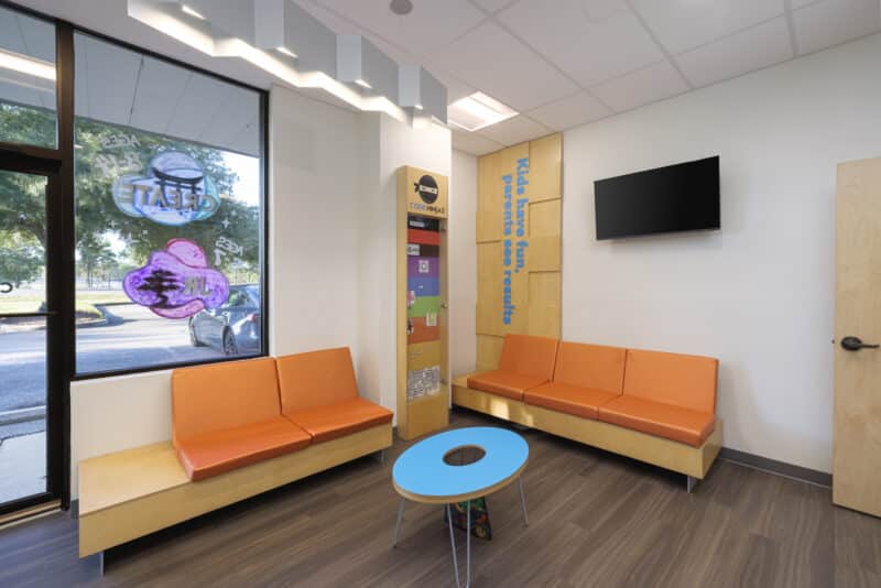Code Ninjas lobby view with lime green accent wall, reception desk, and glass exterior doors.
