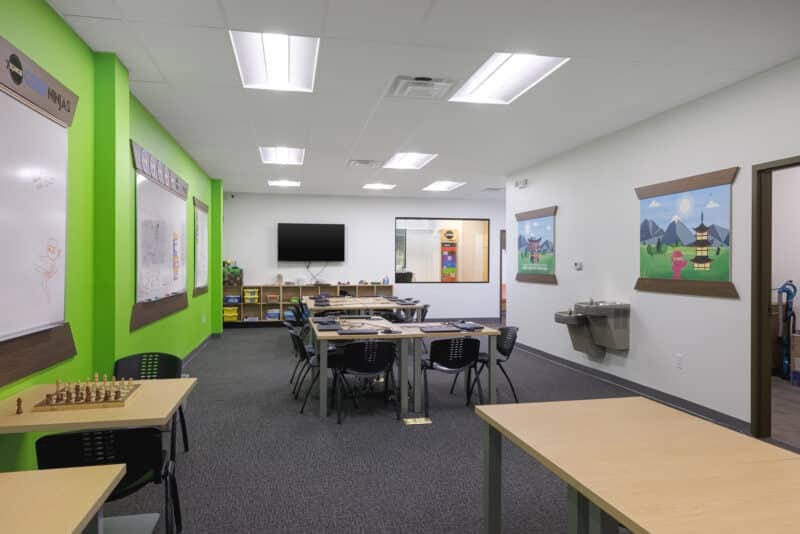 The Code Ninjas Dojo (classroom), featuring bright lime green accent walls, collaborative tables, and wall-mounted whiteboards for coding instruction.