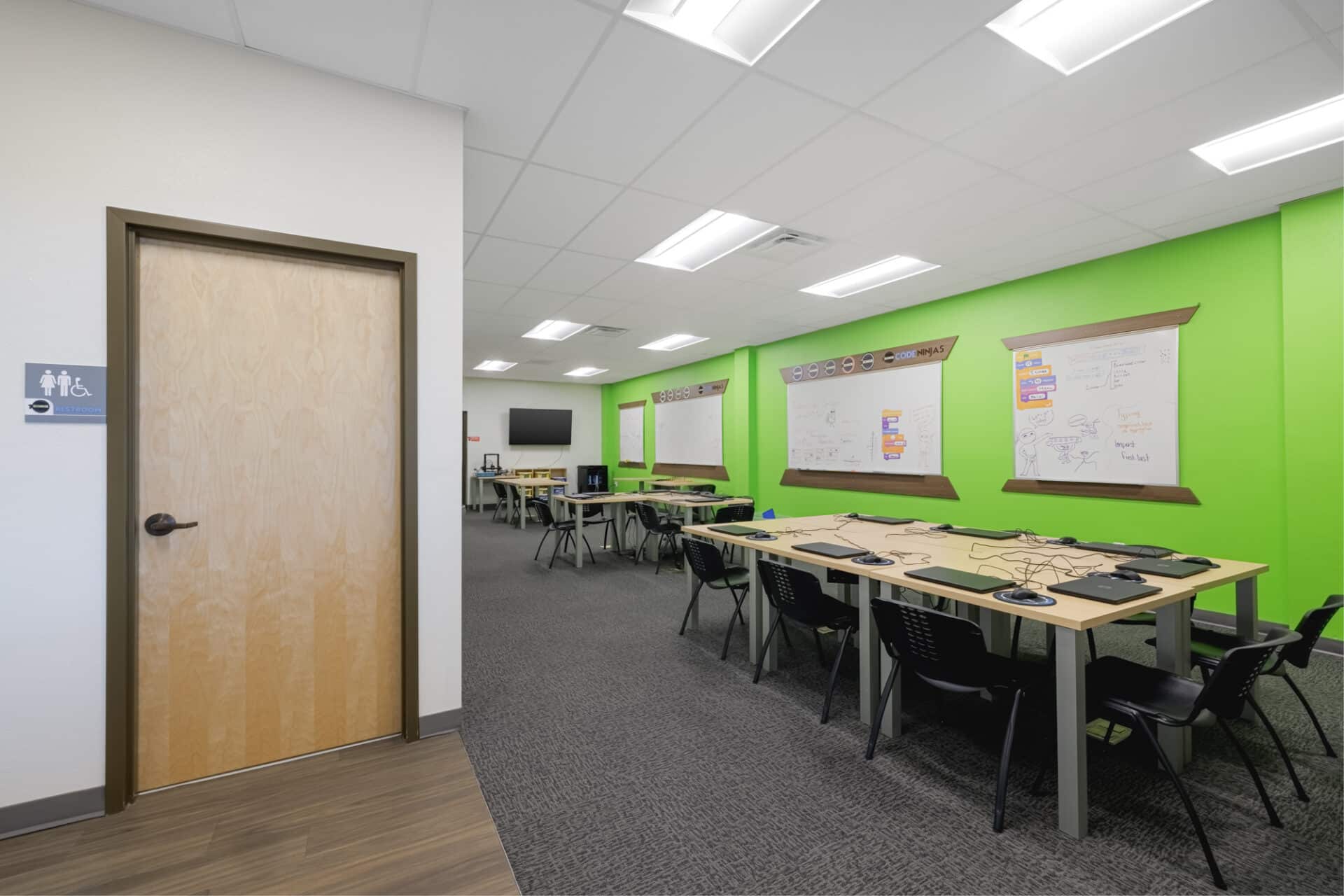 A view of the Dojo from the side, illustrating the arrangement of student tables and the proximity of the clean, light wood restroom access door.