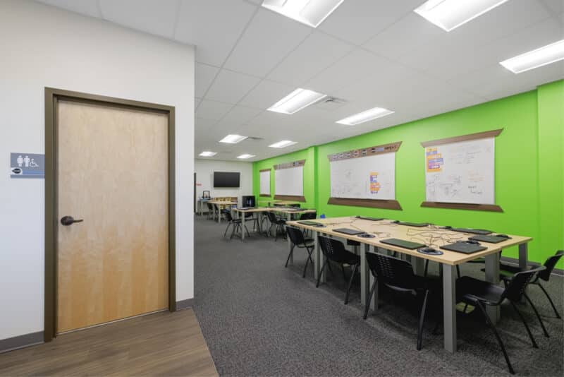 A view of the Dojo from the side, illustrating the arrangement of student tables and the proximity of the clean, light wood restroom access door.