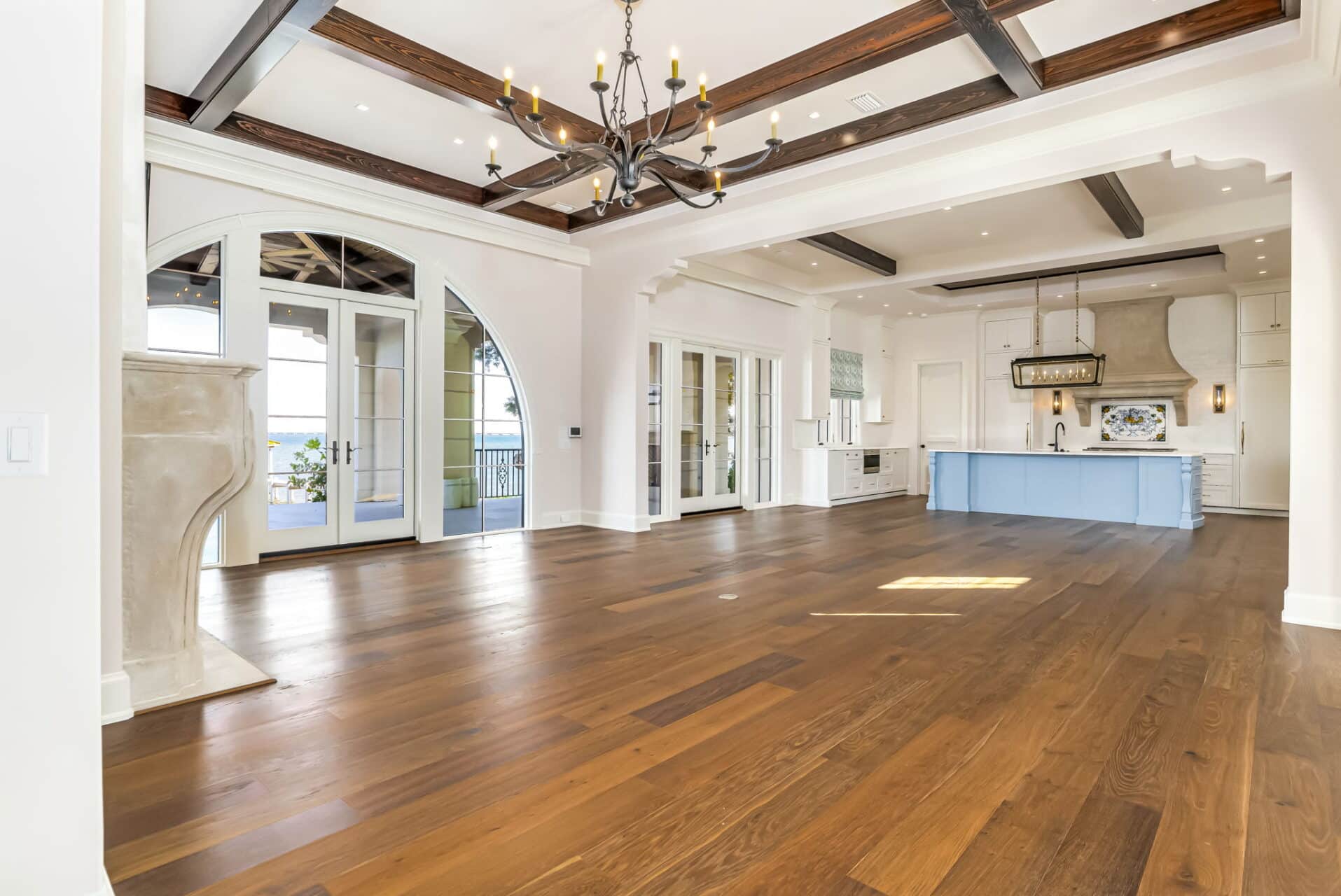 Open-concept great room showing the living area and the adjacent kitchen, featuring a light blue island, white perimeter cabinets, and outdoor views.