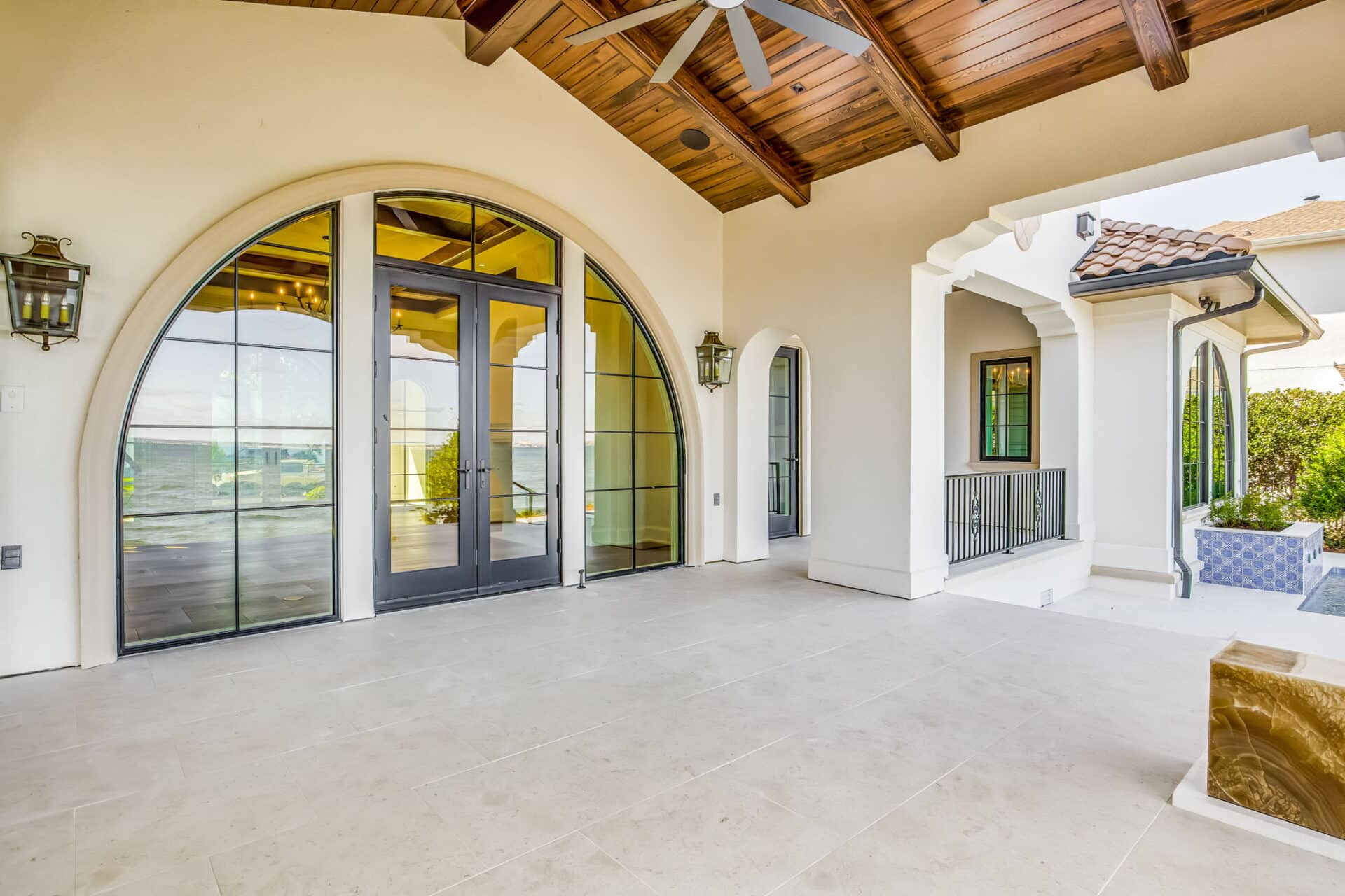 Close-up of the main arched glass doors from the covered patio, flanked by decorative wall lanterns, highlighting the grand scale of the opening.