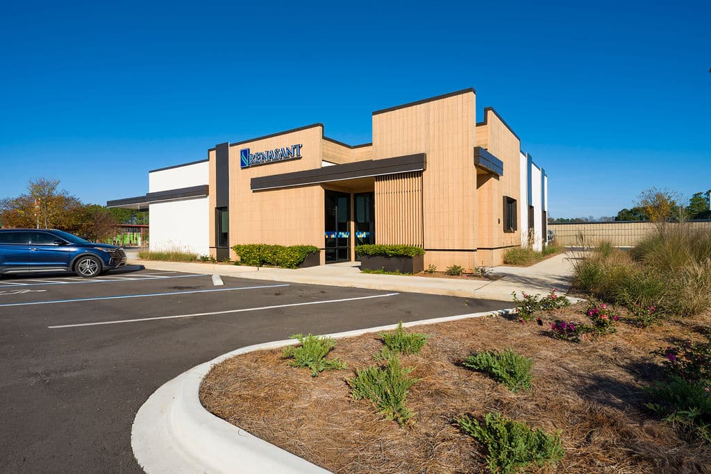 Daytime view of a modern commercial building with tan textured siding and dark metal accents.