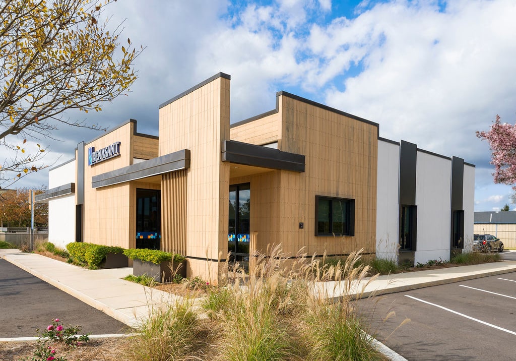 Daytime view of a modern commercial building with tan textured siding and dark metal accents.