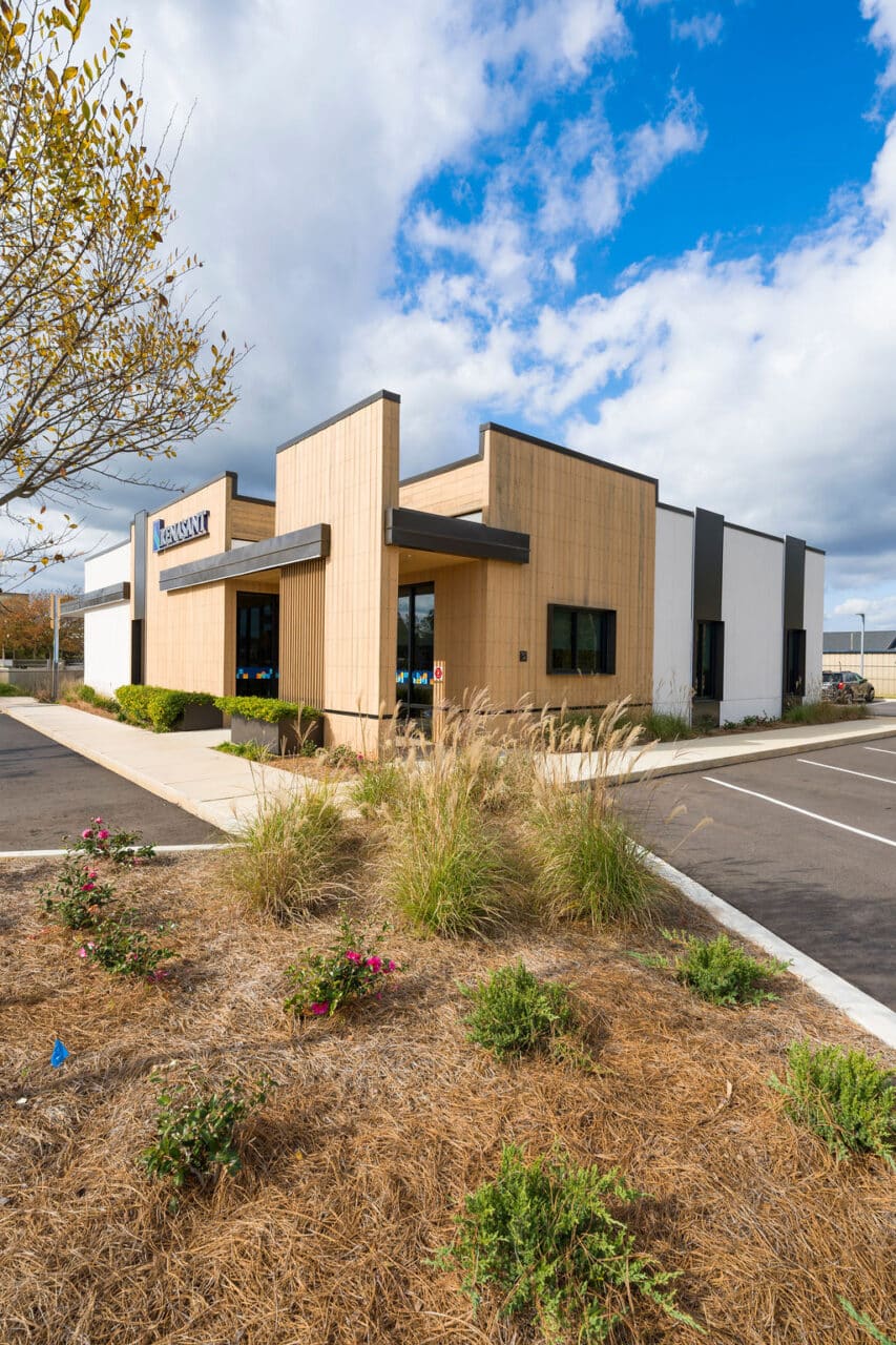 Daytime view of a modern commercial building with tan textured siding and dark metal accents.