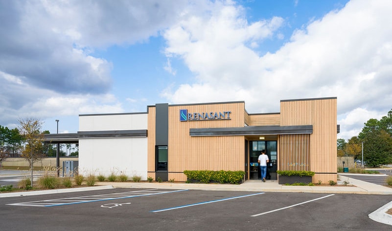 Daytime view of a modern commercial building with tan textured siding and dark metal accents.