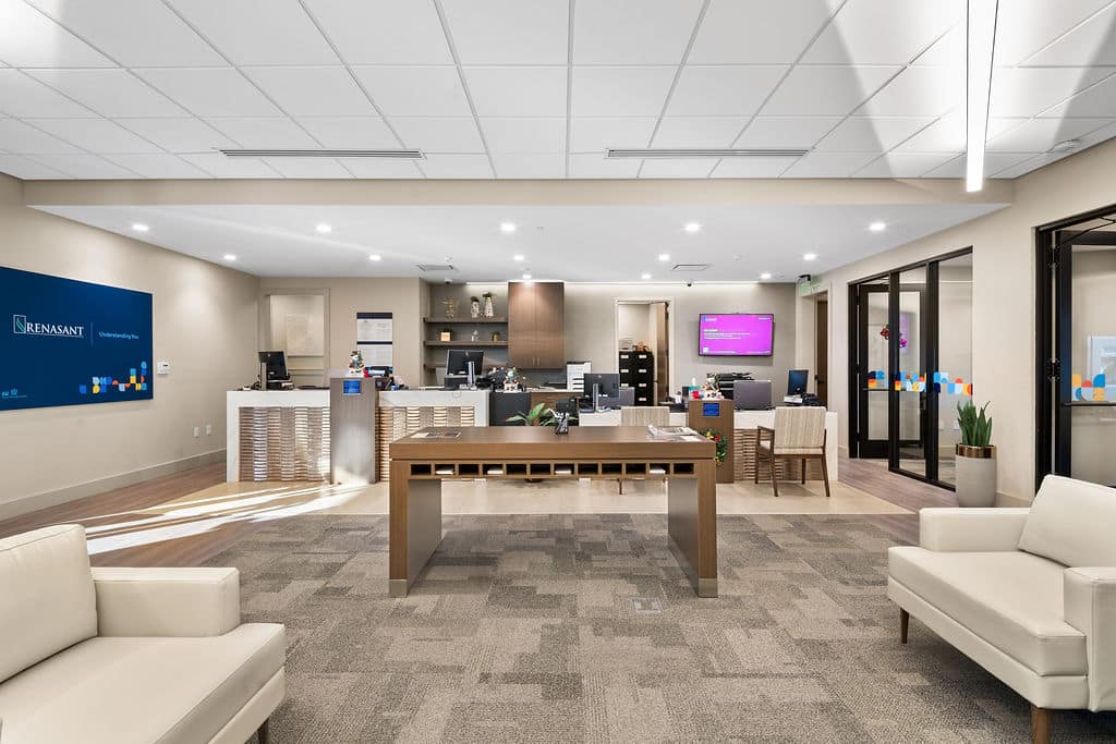 Wide view of the bank lobby featuring teller stations, a central work table, and comfortable seating.