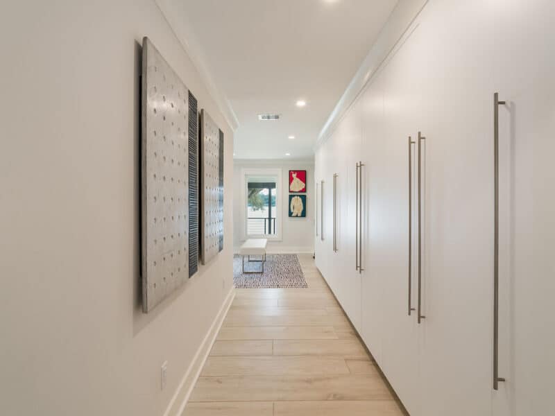 A hallway featuring a wall of white built-in closets with T-bar handles, light wood plank floors, and a view overlooking the water.