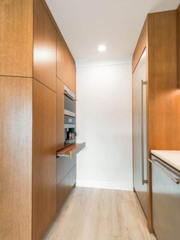 High-end pantry hallway featuring integrated wood cabinetry, a built-in espresso machine with a pull-out shelf, and a stainless steel refrigerator.
