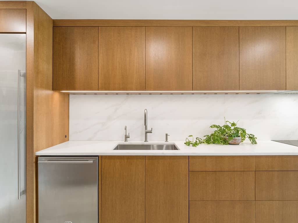 Modern kitchen featuring flat-panel white oak cabinets, a white marble backsplash, and a stainless steel under-mount sink.