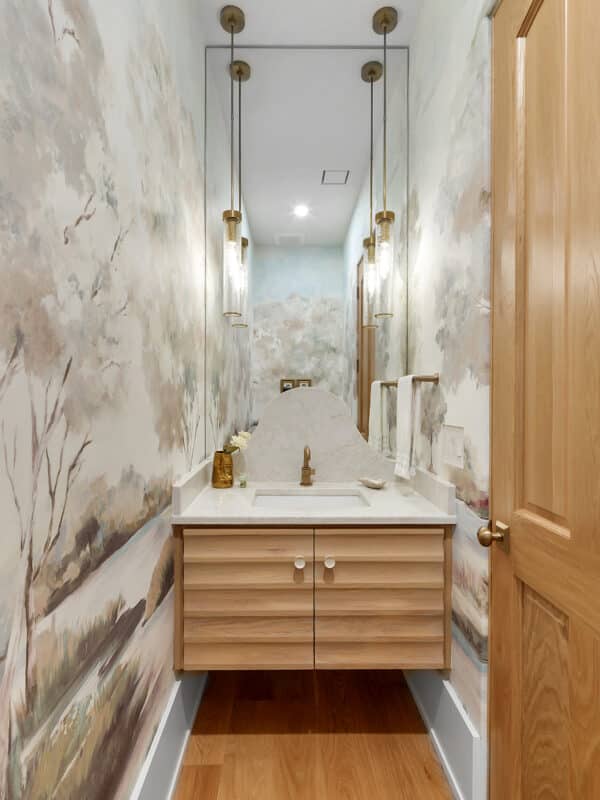 Luxury powder room featuring a custom landscape wall mural, a floating light oak vanity with a fluted facade, an arched marble backsplash, and hanging cylinder pendant lights.