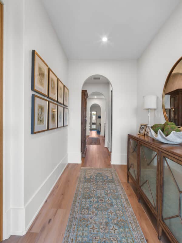 Bright residential hallway with arched doorways, light hardwood floors, and a vintage glass-door console table.