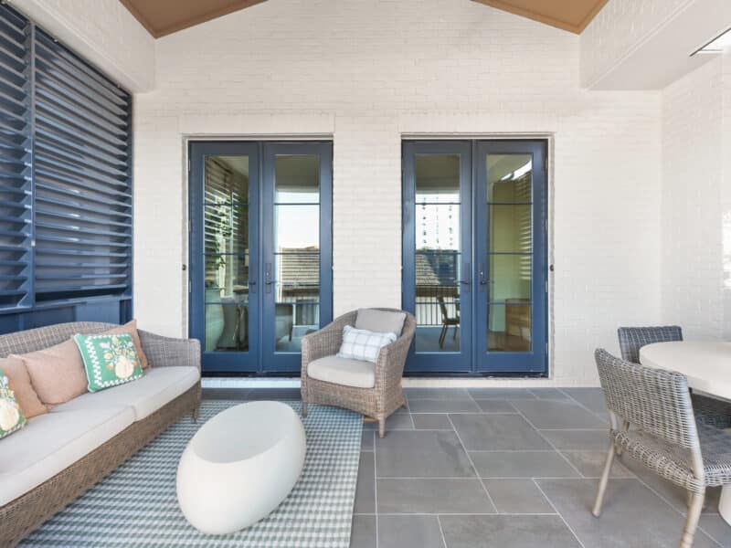 Covered outdoor patio with white brick walls, dark blue French doors, a white coffee table, a white cushioned sofa, and an outdoor dining set.