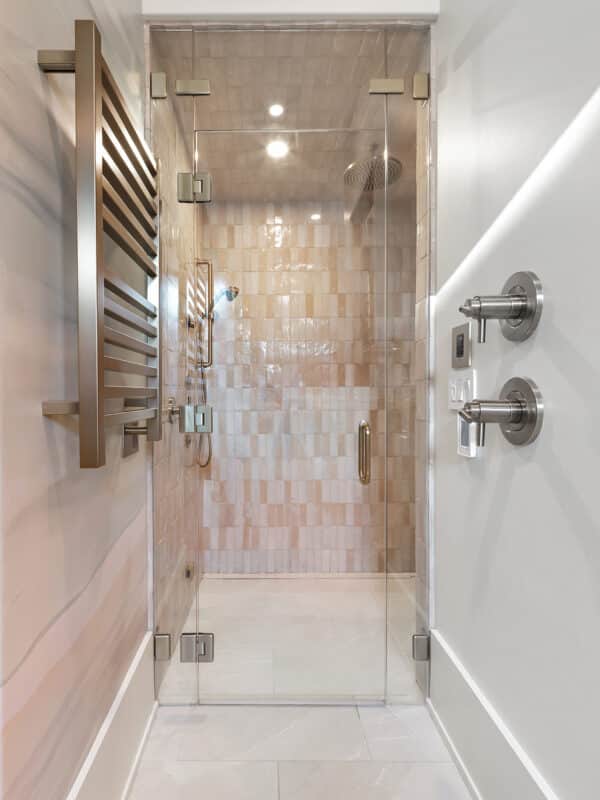 Modern luxury walk-in shower with a frameless glass door, glossy vertical beige tiles, a rainfall showerhead, and a wall-mounted stainless steel towel warmer.