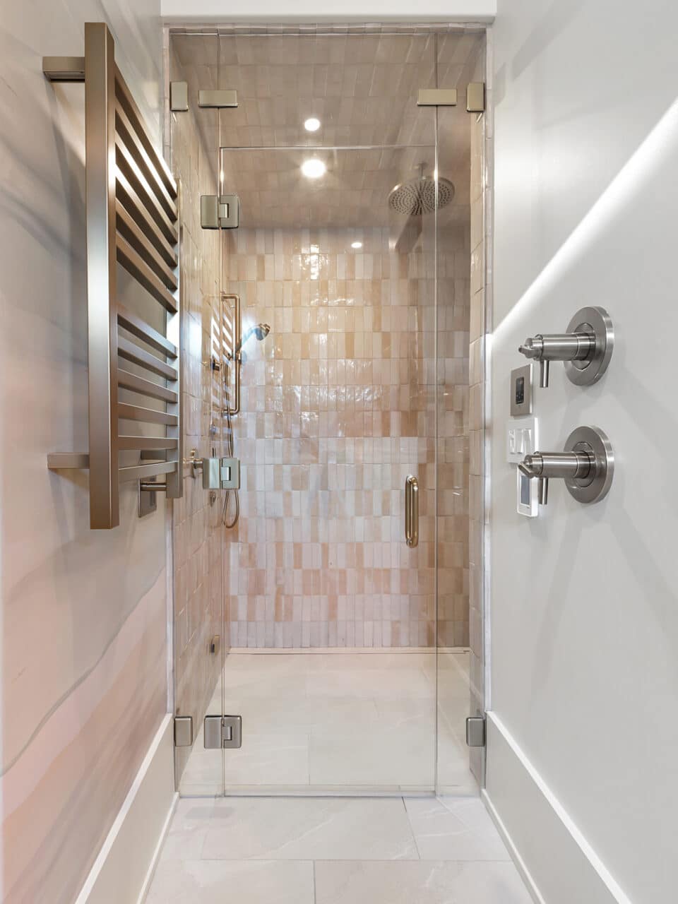 Modern luxury walk-in shower with a frameless glass door, glossy vertical beige tiles, a rainfall showerhead, and a wall-mounted stainless steel towel warmer.