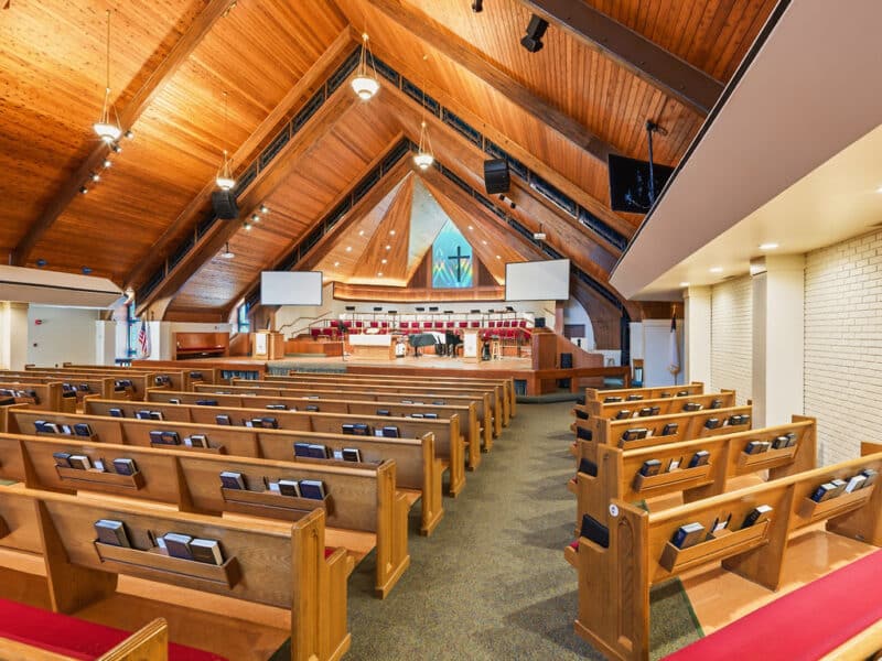 Right-angle interior view of a church featuring wooden pews, white brick accent walls, and a vaulted timber ceiling.
