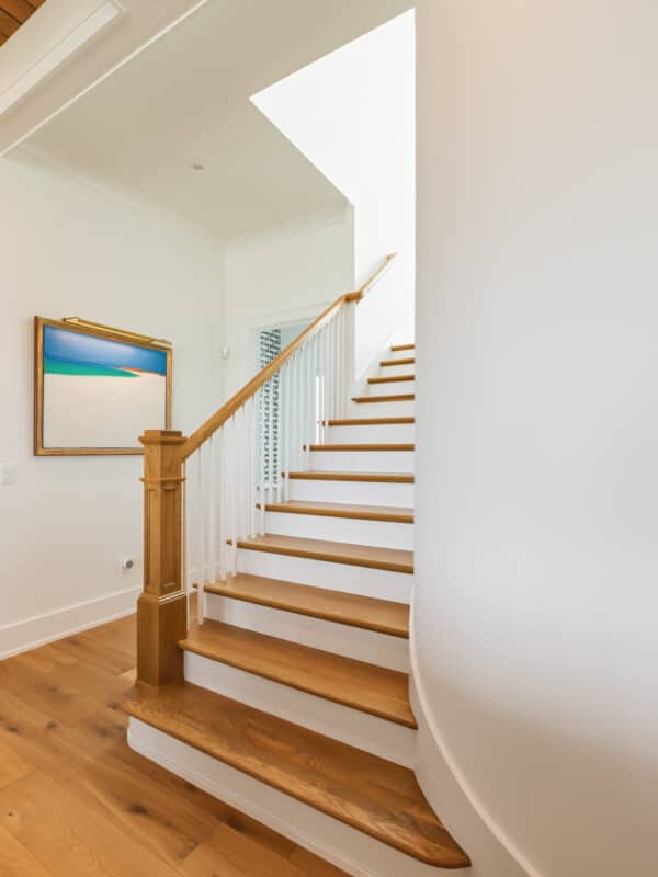 Modern interior staircase with light oak wood treads, white risers, a matching oak handrail, and white spindles against bright white walls.