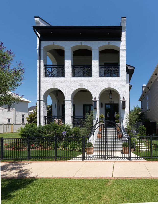 Front exterior of a luxury two-story white brick custom home featuring triple-arched entry porches, black wrought iron railings, and a matching black security gate.
