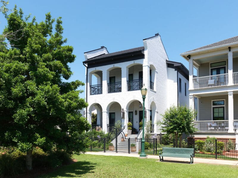 Front exterior view of a luxury two-story white brick house featuring arches, black wrought-iron balcony railings, and ornamental landscaping.