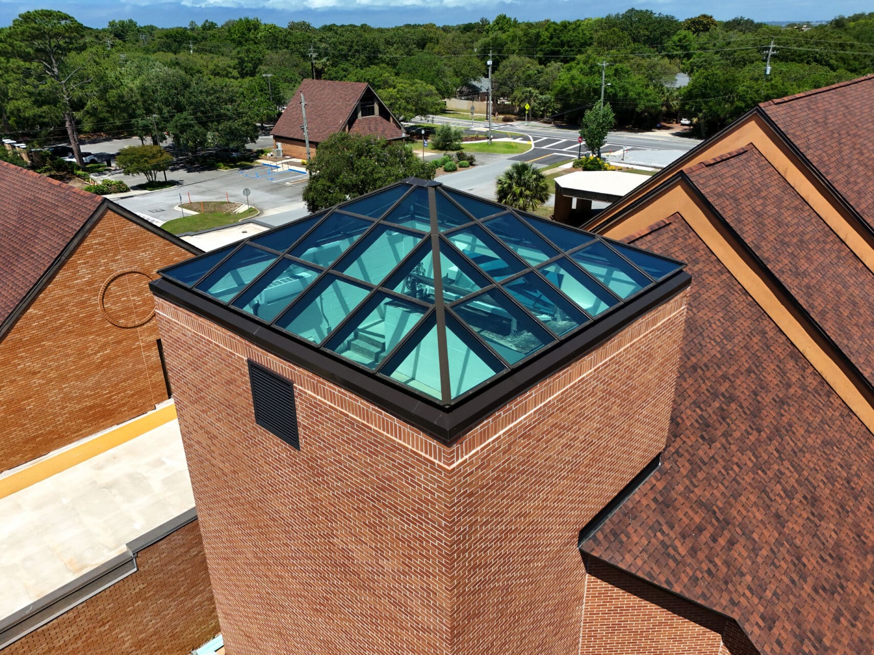 Close-up of a pyramid-shaped architectural glass skylight with a dark metal frame on top of a red brick tower.