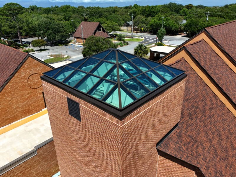 Close-up of a pyramid-shaped architectural glass skylight with a dark metal frame on top of a red brick tower.