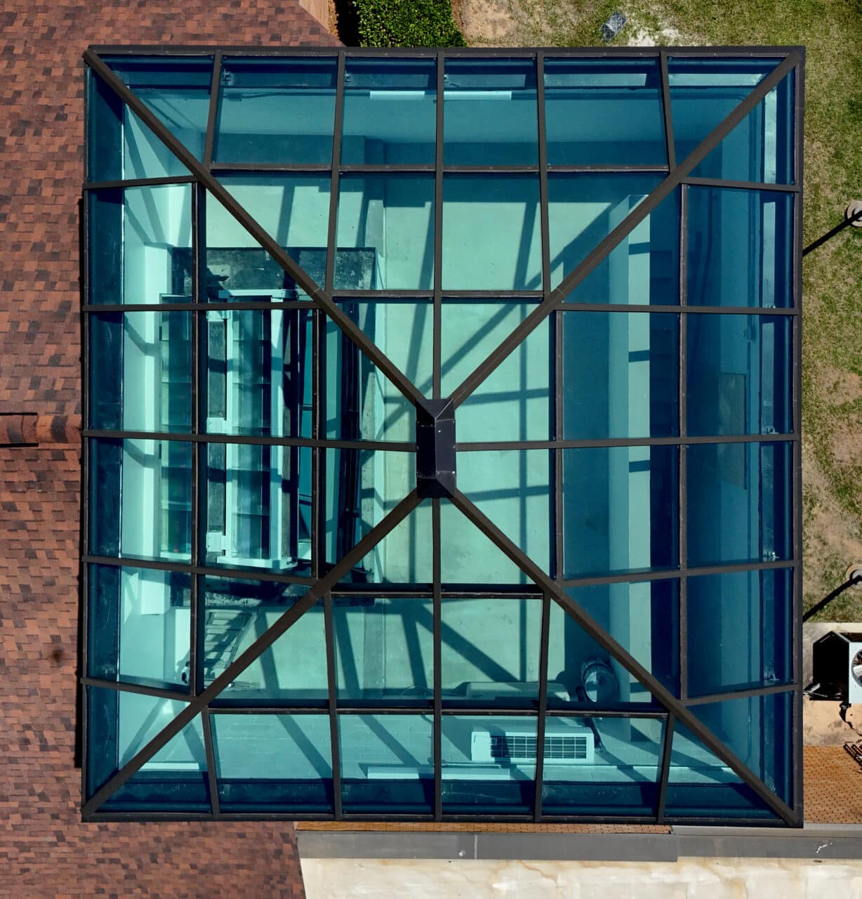 Directly overhead bird's-eye view looking down through a symmetrical square pyramid glass skylight with a dark grid frame.