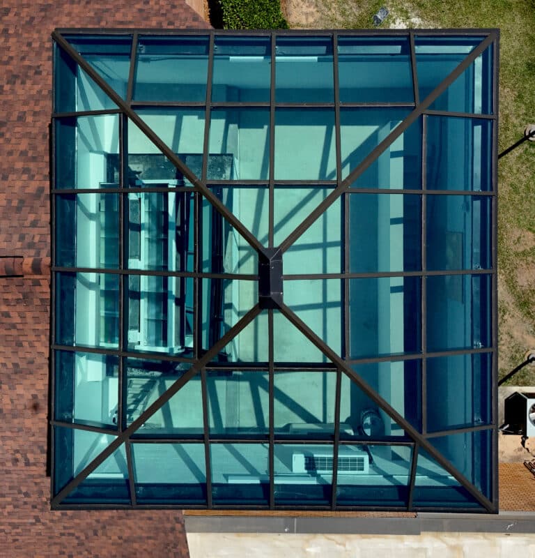 Directly overhead bird's-eye view looking down through a symmetrical square pyramid glass skylight with a dark grid frame.