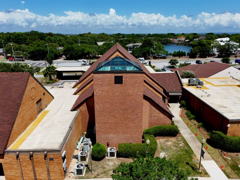 A brick church featuring a central tower topped with a large pyramid glass skylight for a prism and brown shingled roofs.